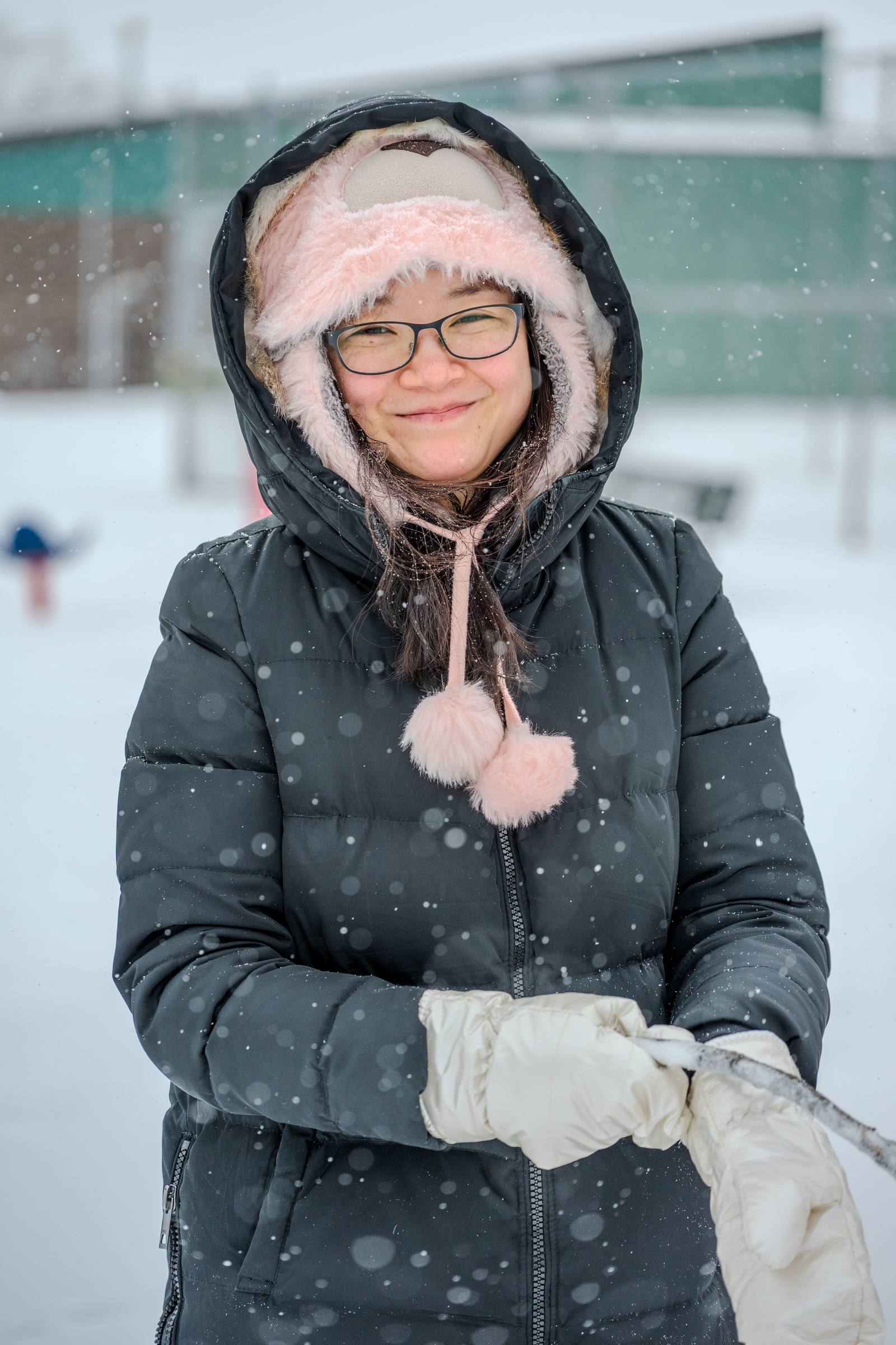 A person in a winter coat standing outdoors as snow falls.