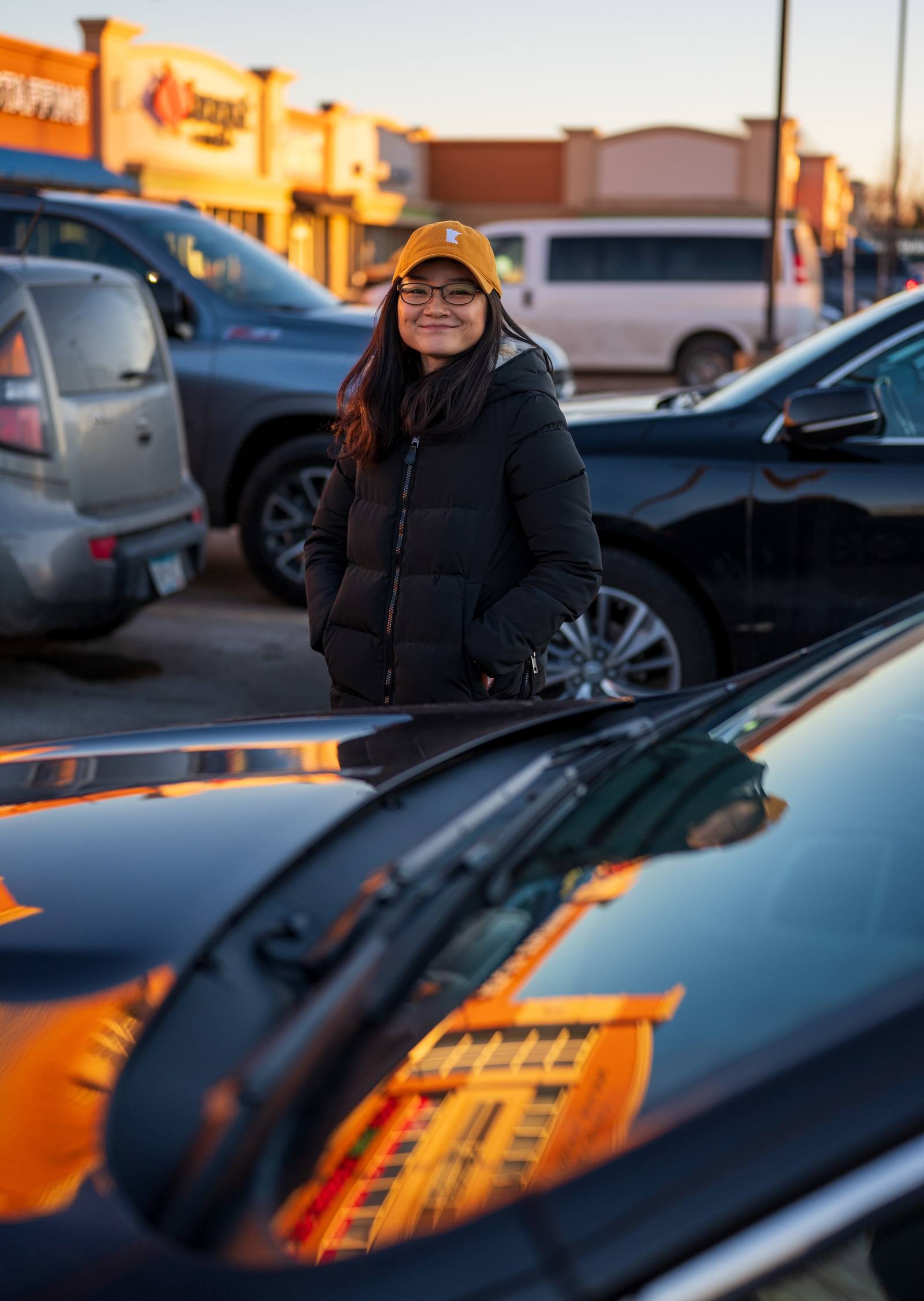 A person standing beside parked cars with warm reflections across the hood.
