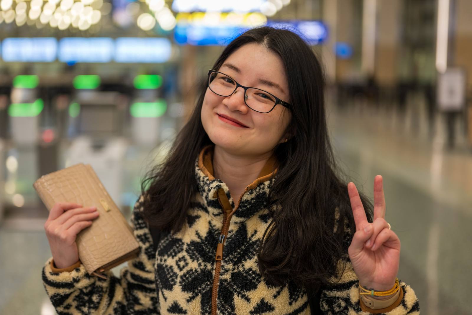A smiling person holding a notebook and flashing a peace sign indoors.