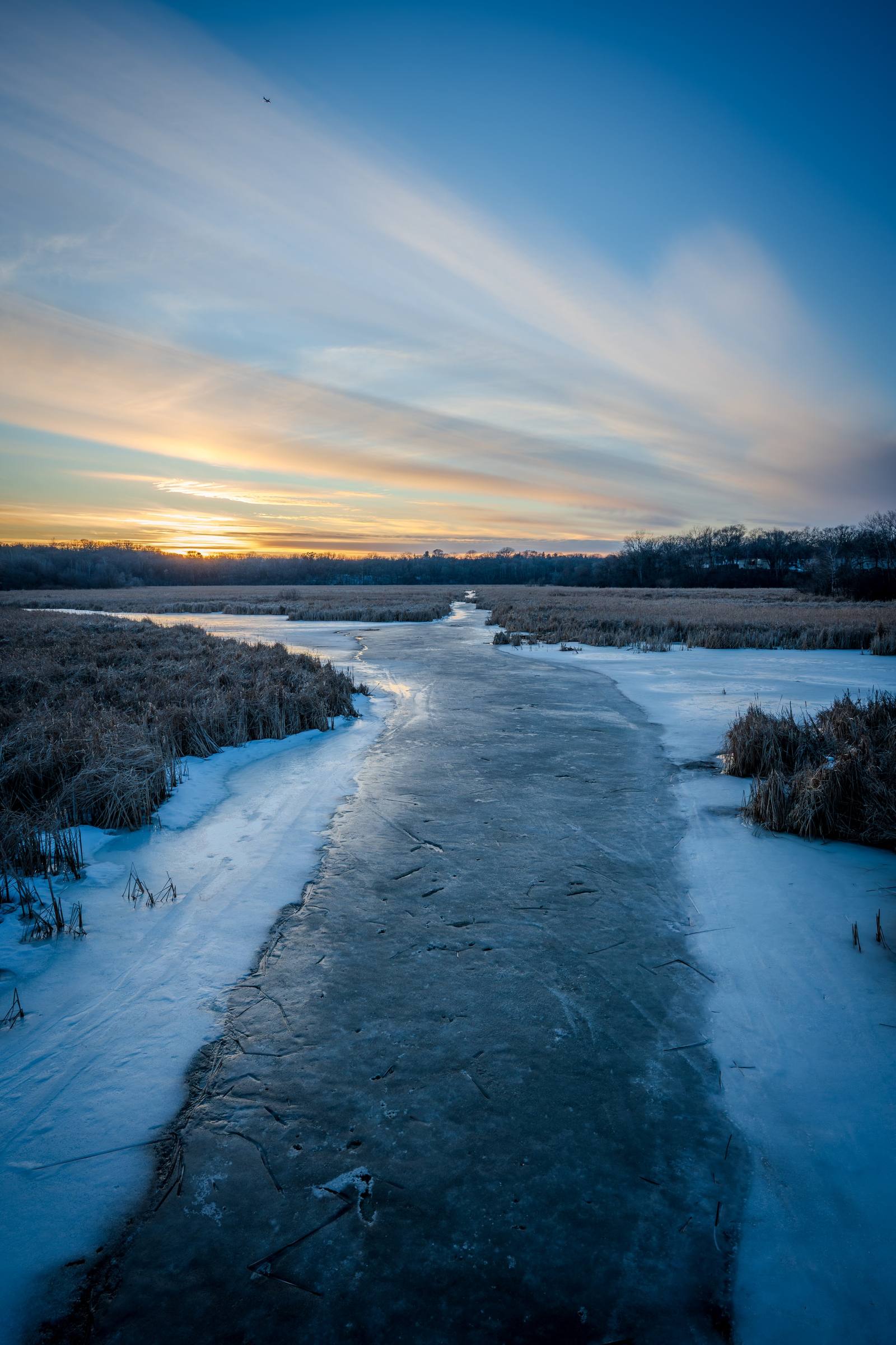A frozen river winding through a snowy landscape at sunset.
