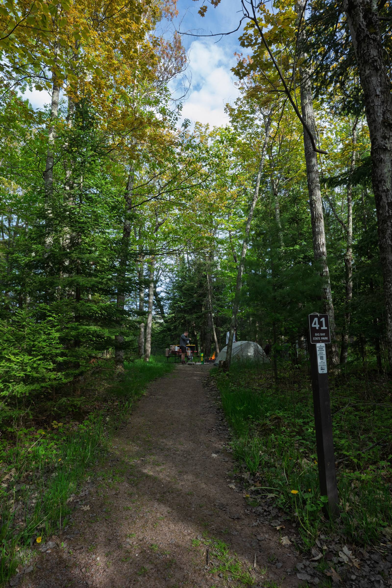 A wooded dirt path leads to campsite 41 at Big Bay State Park, with a dome tent and camp table visible through the trees in the distance.